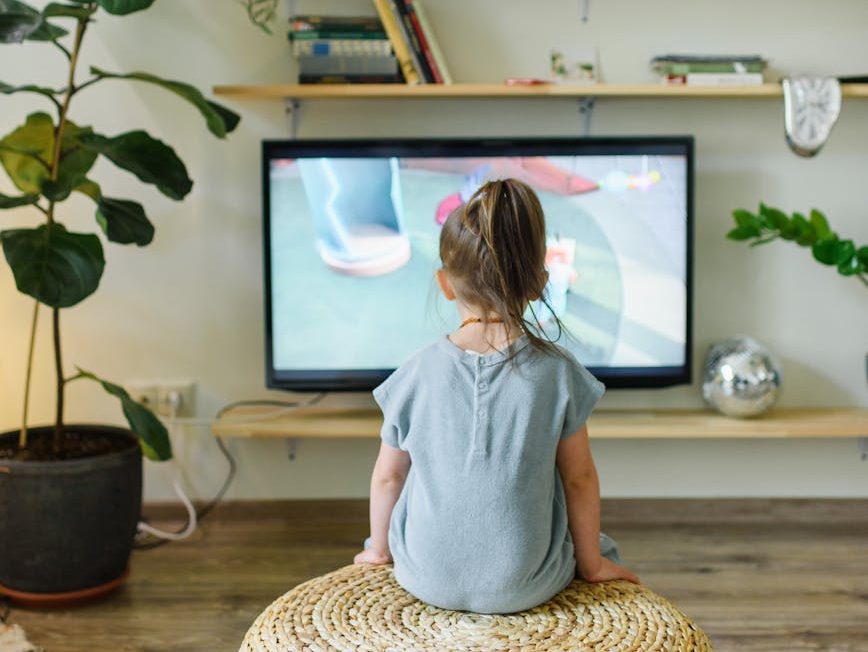 faceless girl watching tv on wicker stool at home