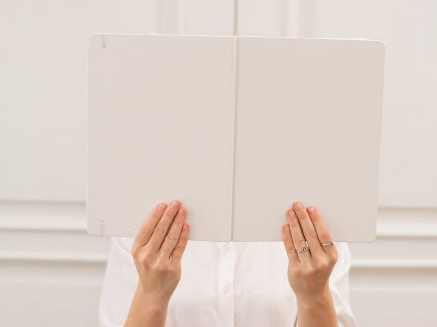 unrecognizable woman covering face behind blank book